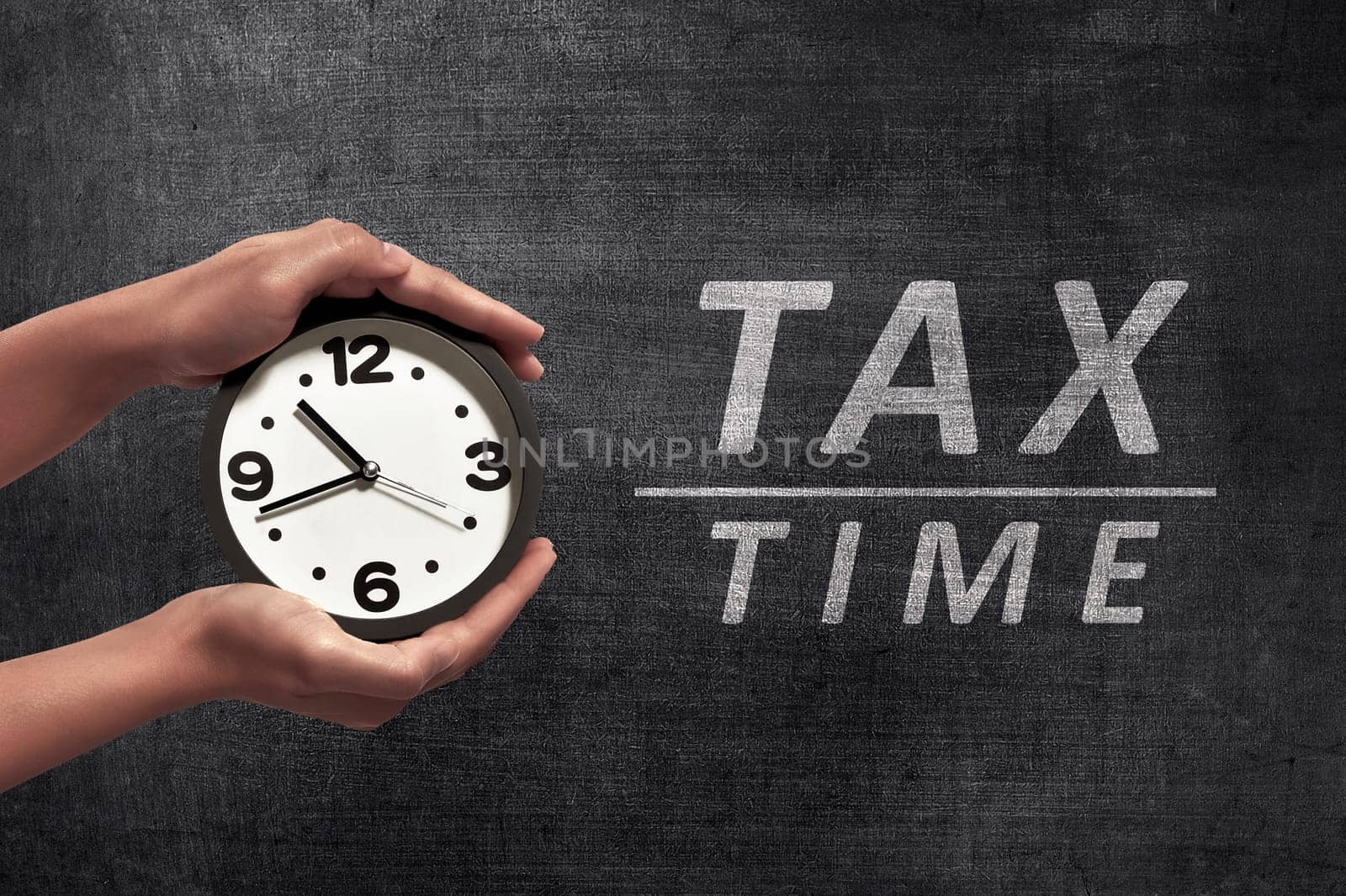People hand holding black alarm clock beside Tax time announcement on blackboard