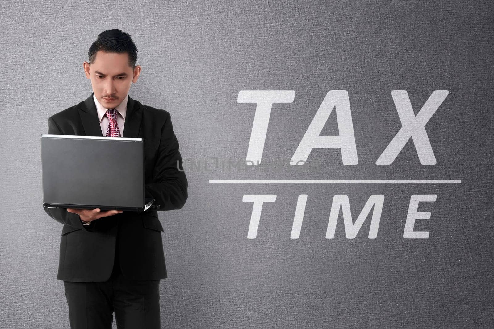 Young asian businessman working on laptop with TAX TIME text on the wall
