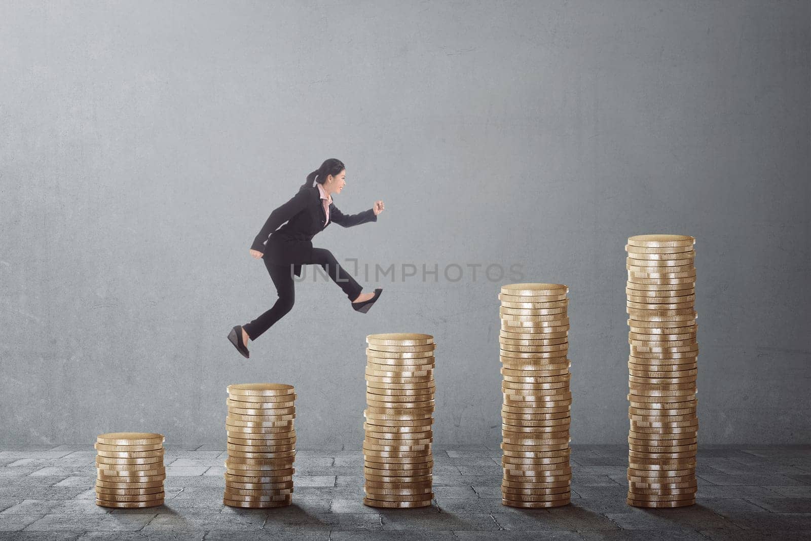 Young asian business woman climb up the gold coins on a grey background
