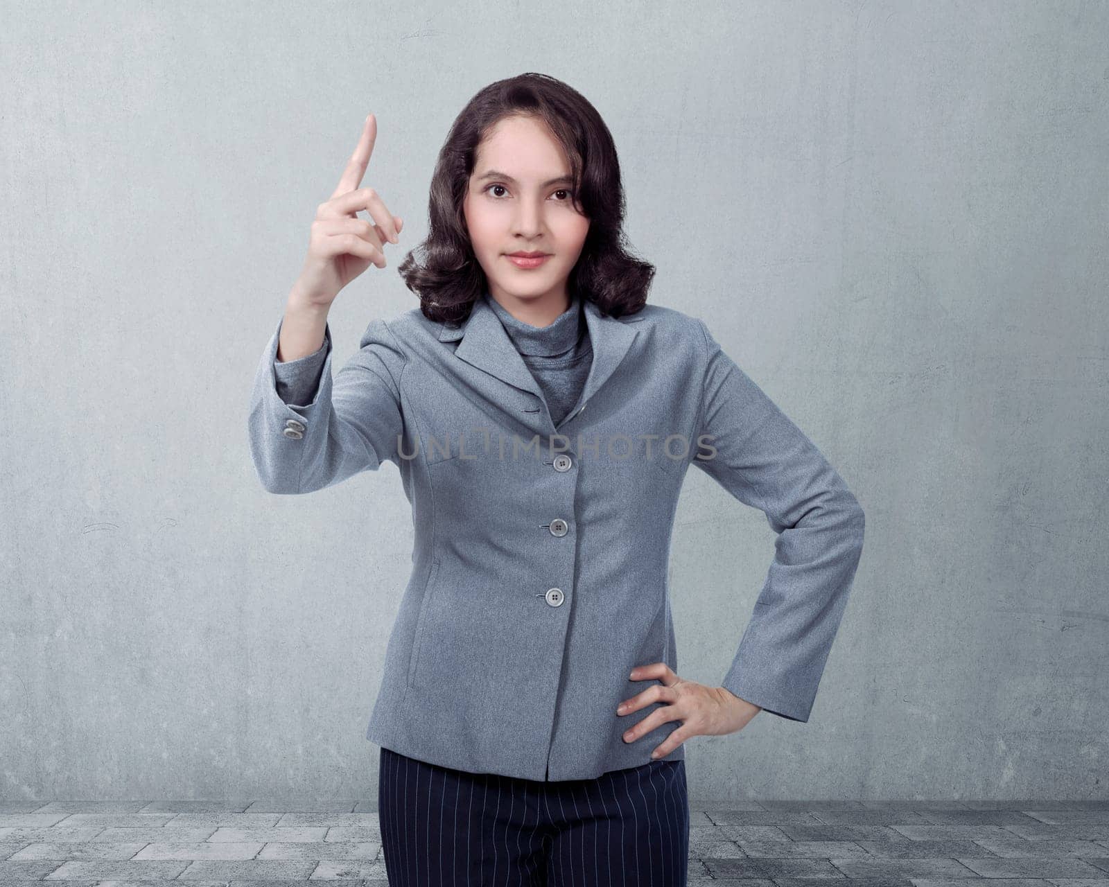 Asian business woman pointing something over gray wall background