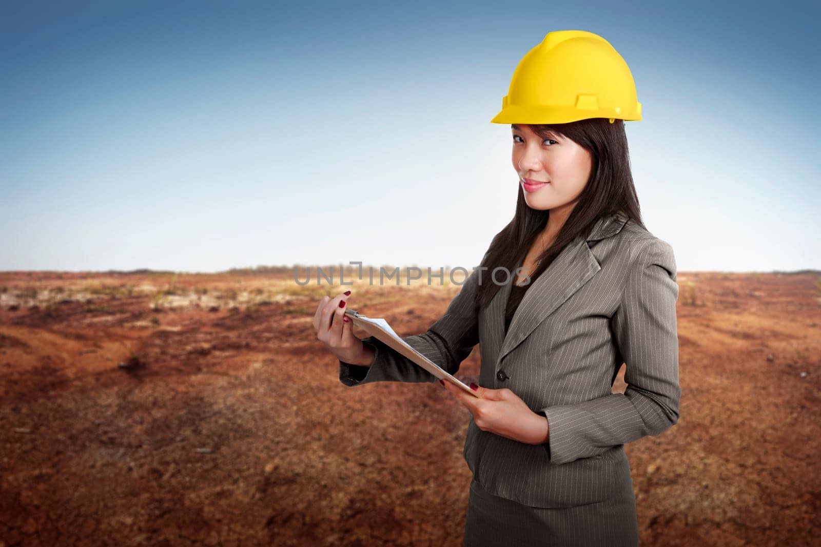 Happy asian contractor woman holding blueprint on clipboard at construction site