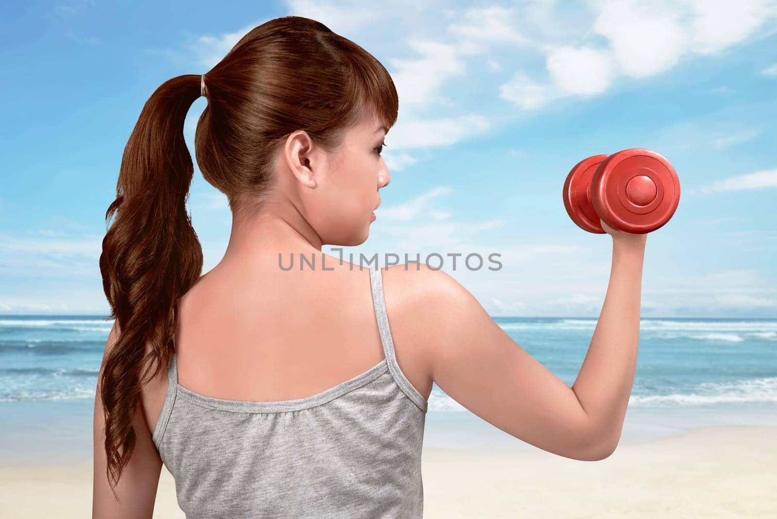Attractive asian woman works out with dumbbells as a fitness on the beach