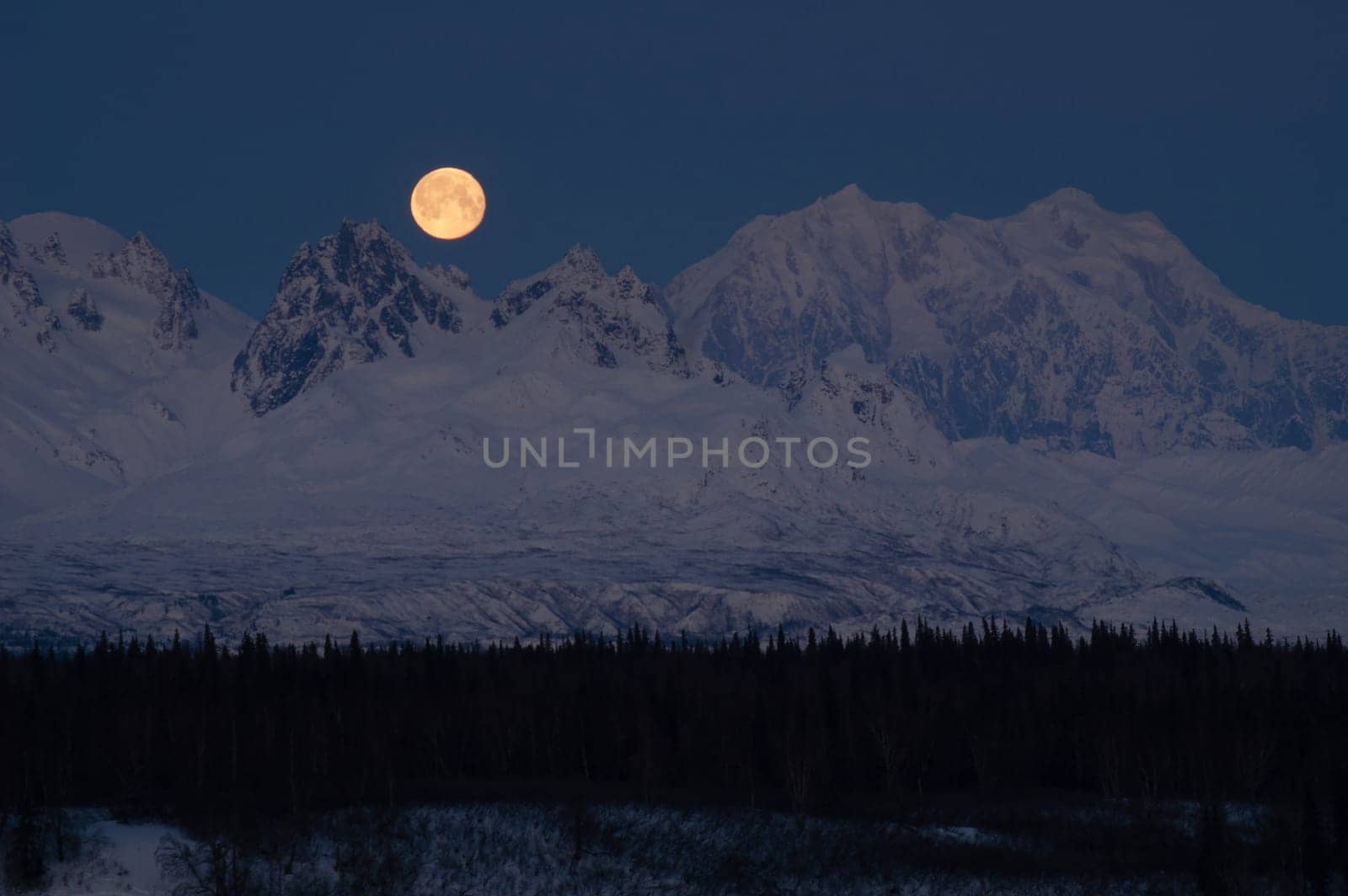 The moon emerges from behind the mountains in Denali