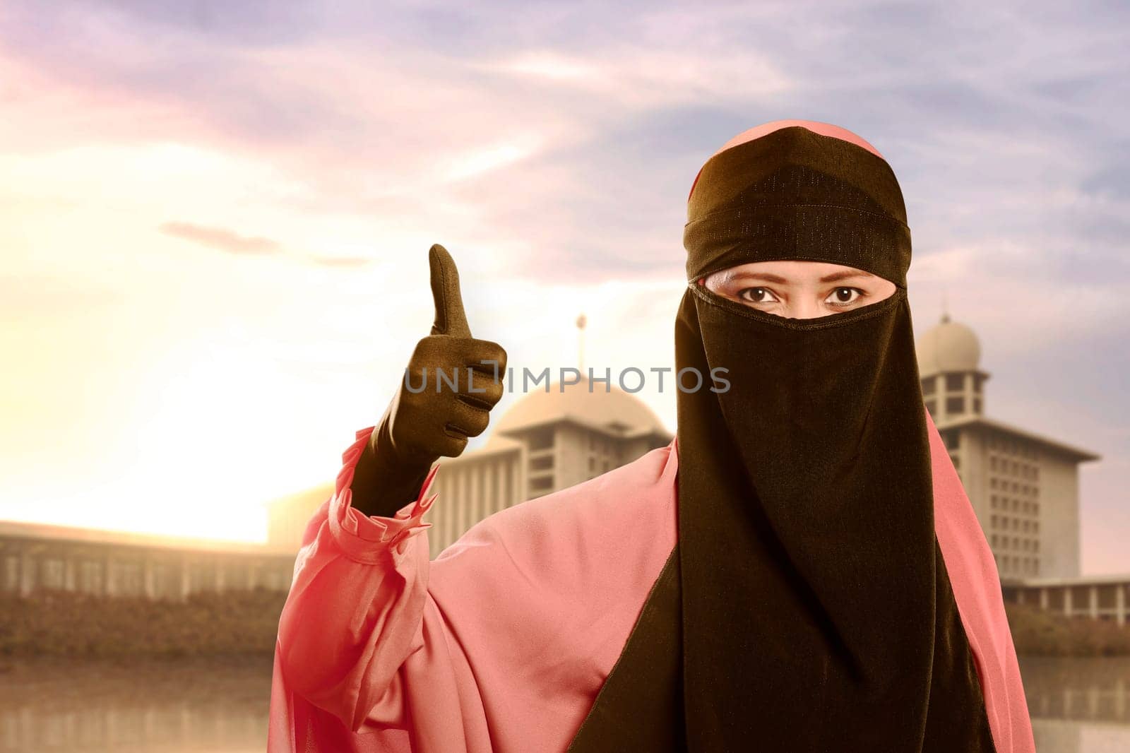 Beautiful asian muslim woman with niqab showing thumbs against mosque background