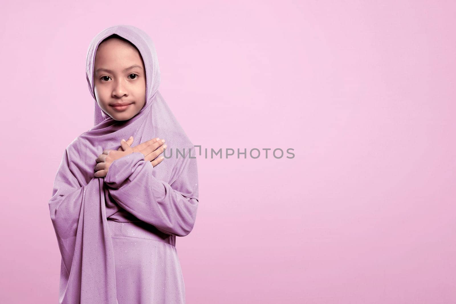 Small asian muslim girl in hijab with peaceful expression over pink background