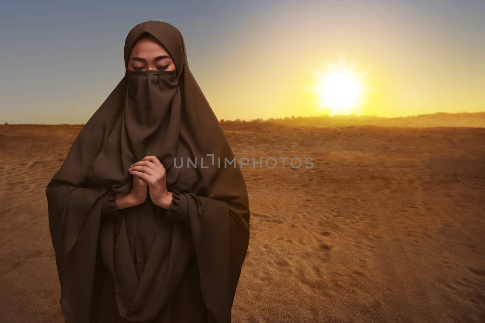 Portrait of asian muslim woman in niqab clothes praying during sunset