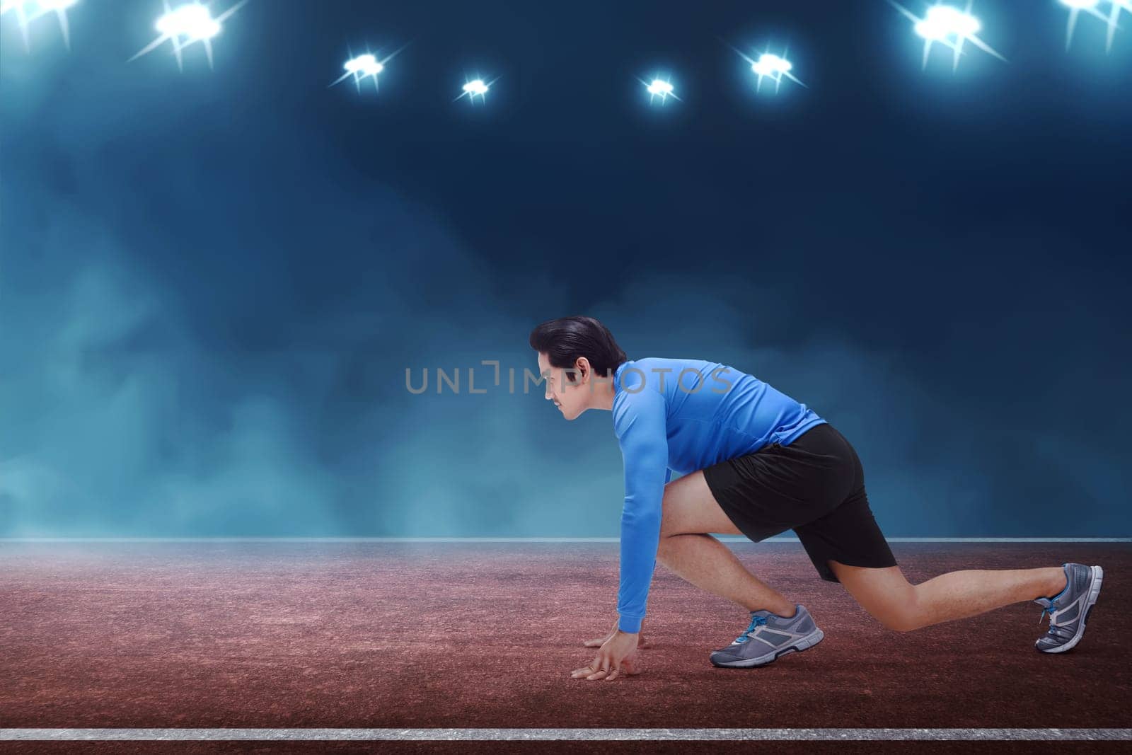 Young asian runner man kneeling ready in start position on race track