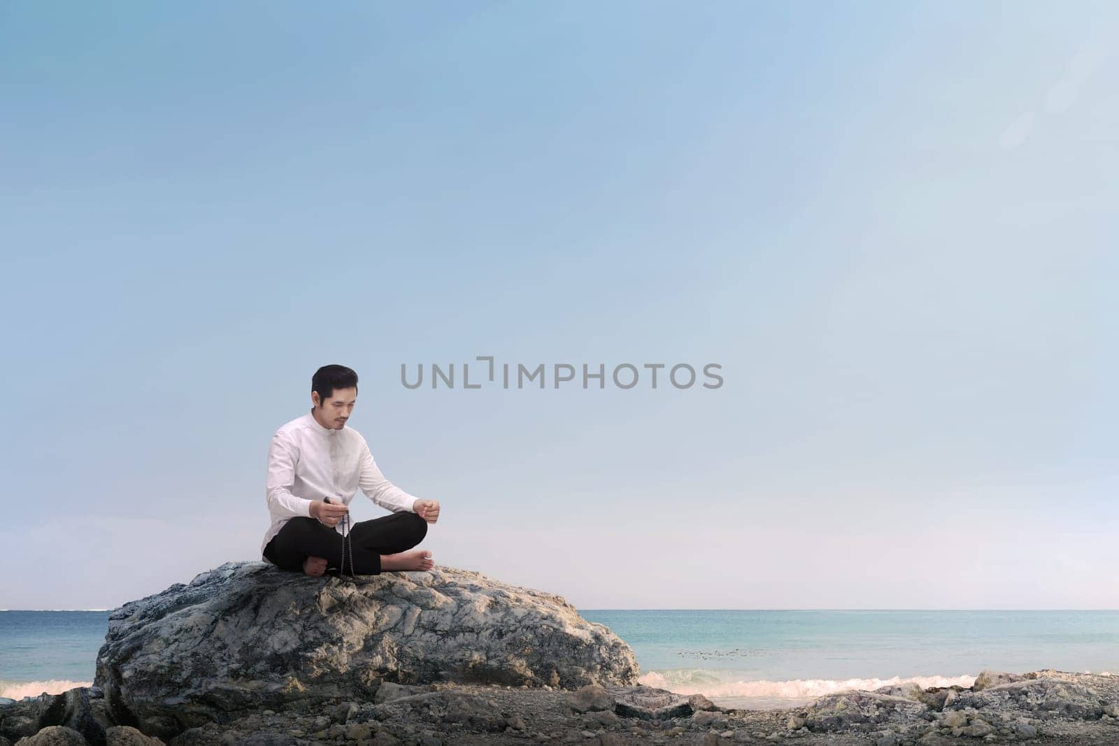 Handsome asian muslim man praying with prayer beads on the beach