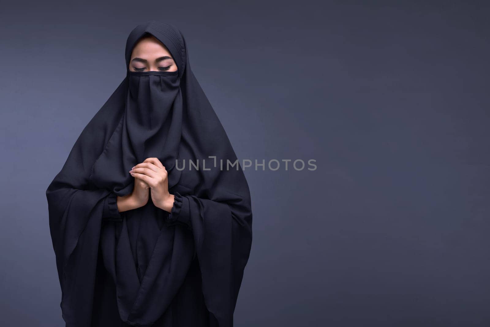 Young asian muslim woman wearing niqab praying with dark background