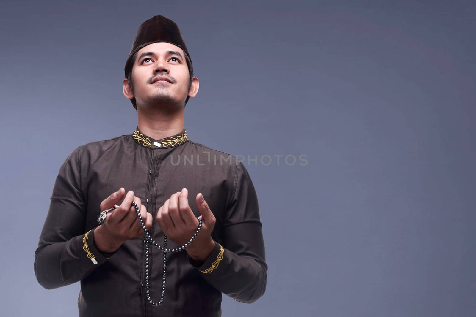 Young asian muslim man praying with prayer beads against dark background