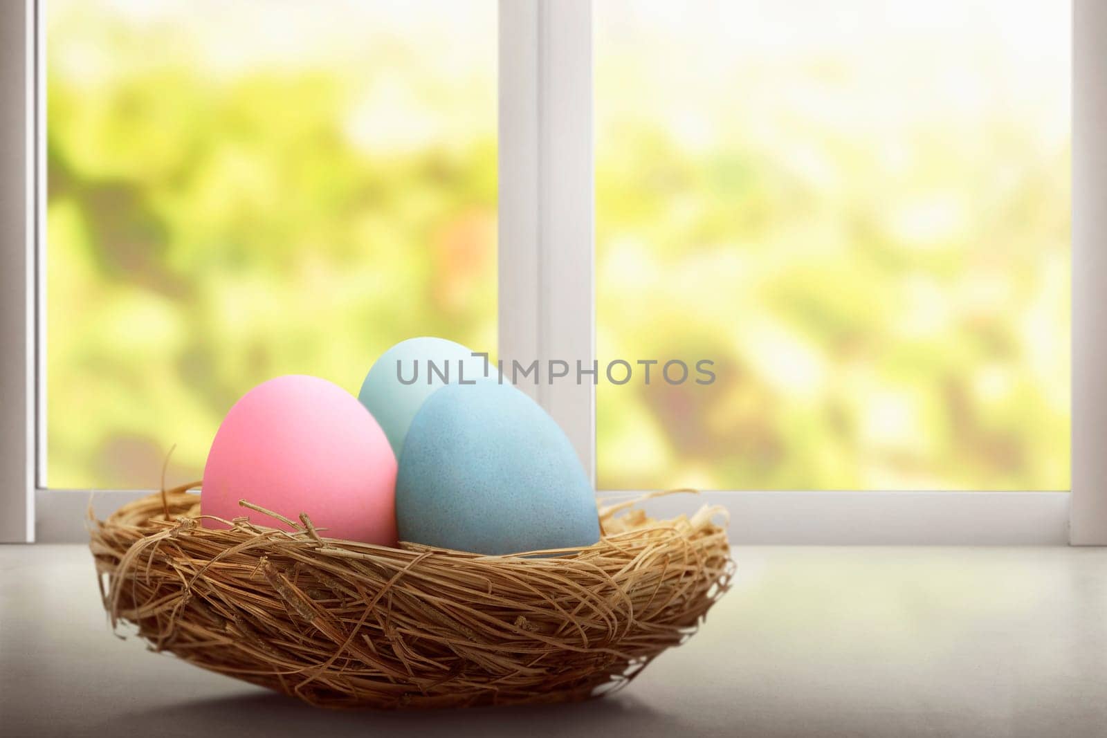 Colorful easter eggs in nest at desk in front of window background