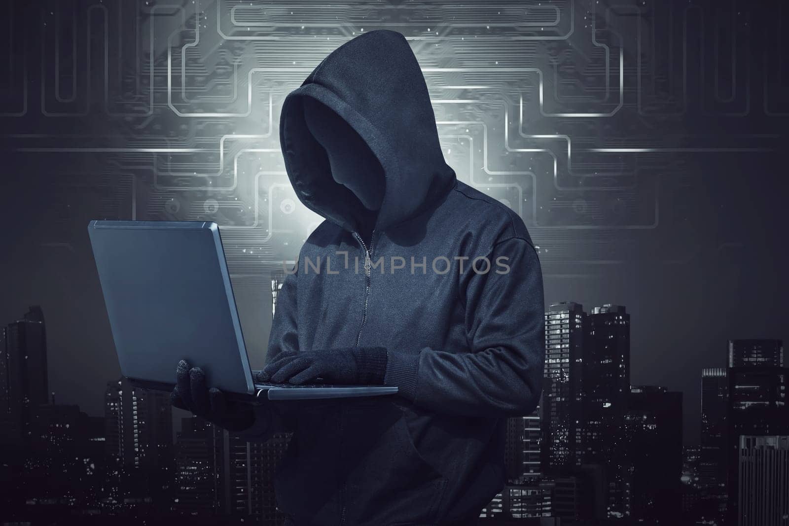 Hooded hacker holding laptop while typing against digital city background