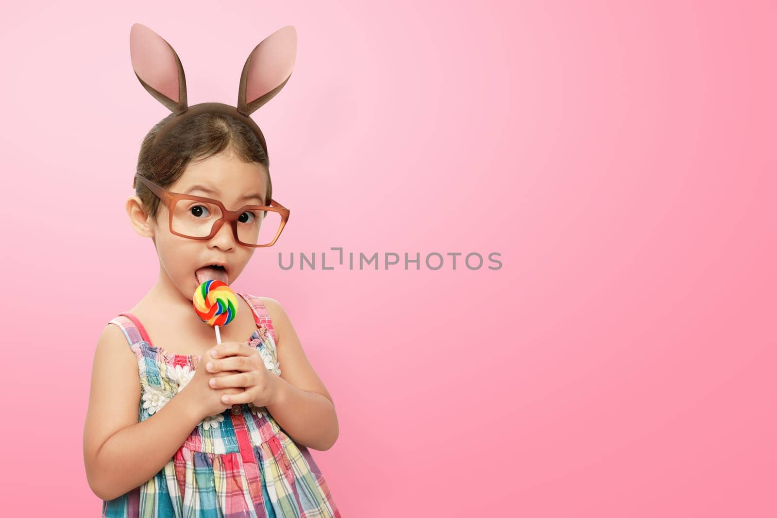 Smiling asian child girl wearing bunny ears on Easter day against pink background