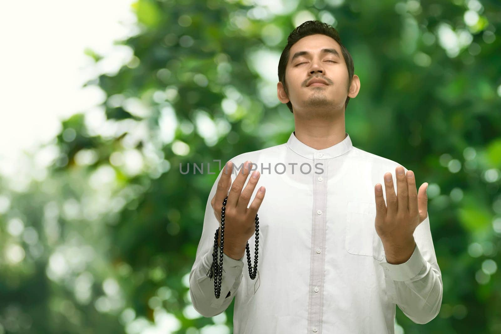 Young asian muslim man praying with prayer beads in the outdoor