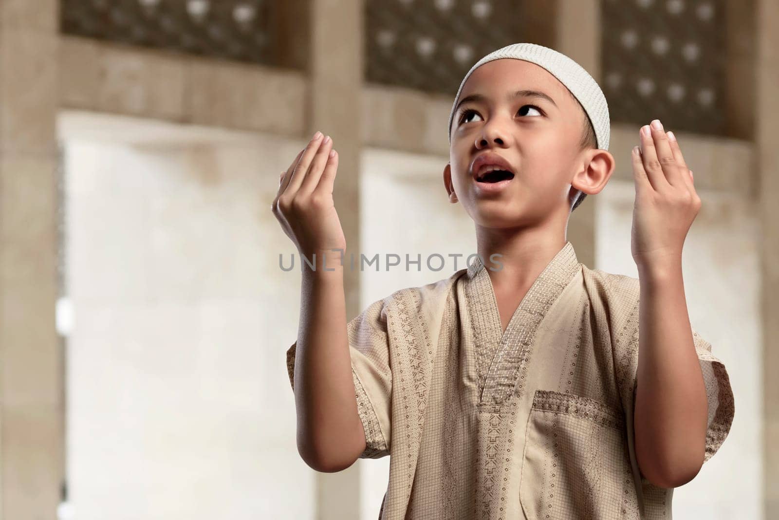 Little asian muslim boy is praying with raise hand in the mosque