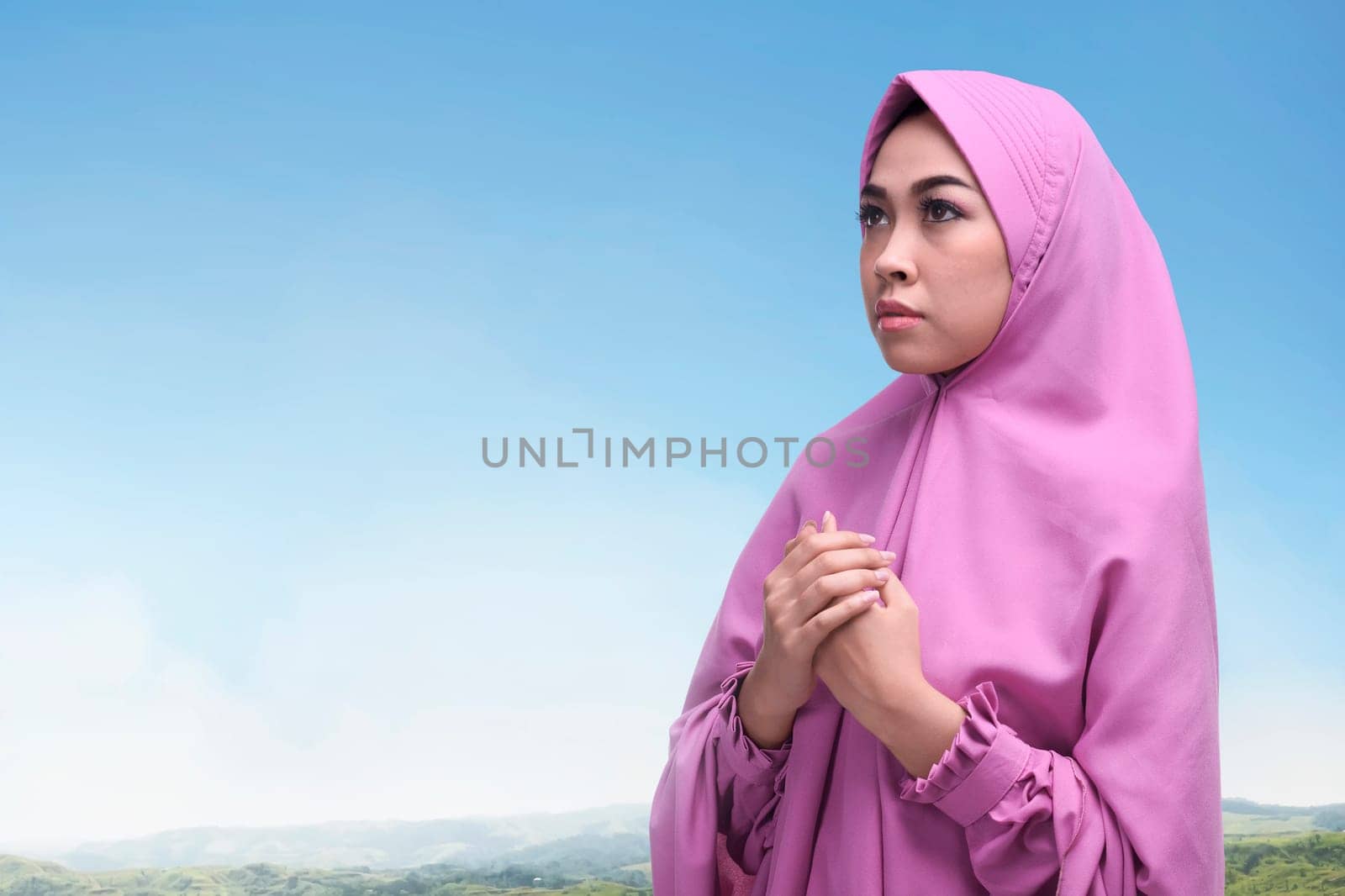Young asian muslim woman raised both her hand to praying with blue sky background