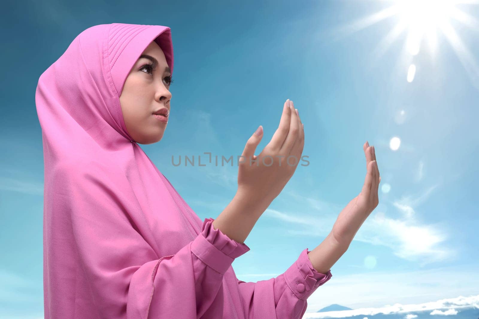 Young asian muslim woman in hijab dress praying against blue sky background