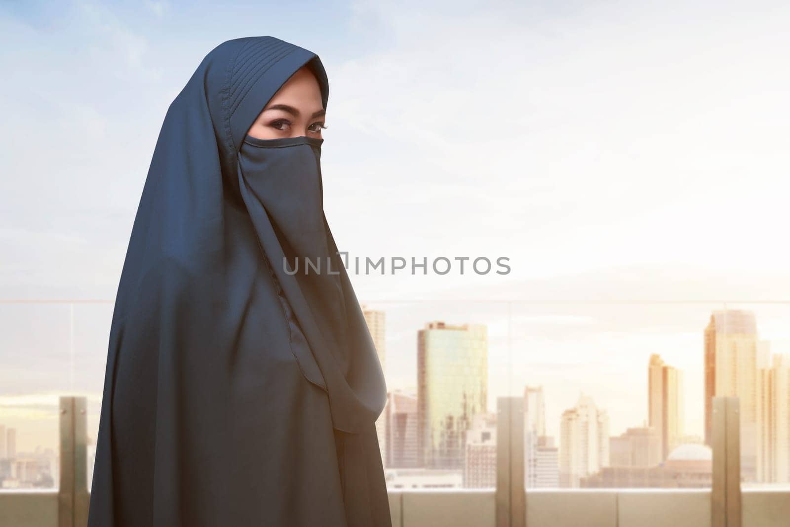 Religious asian muslim woman with covered face standing against cityscape background