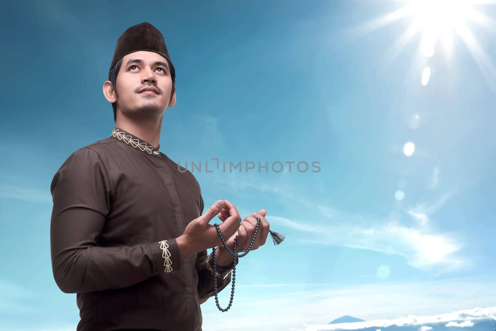 Young asian muslim man with prayer beads pray to god over blue sky background