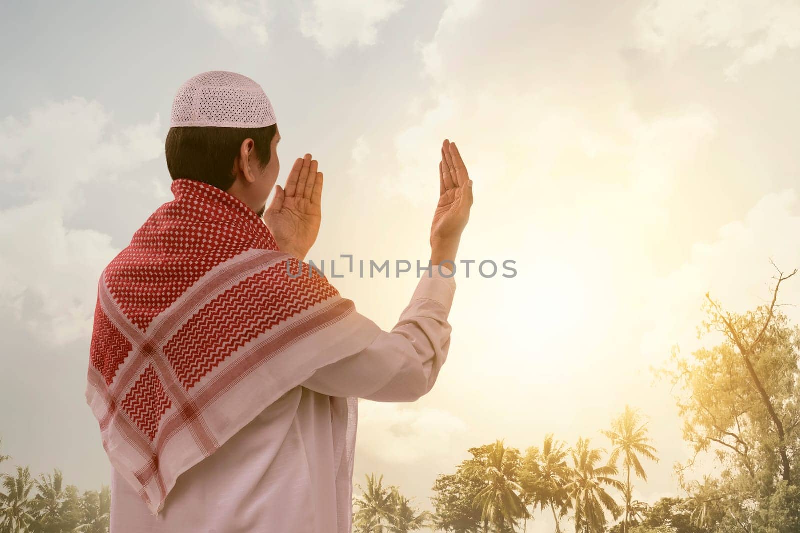 Back view of asian muslim man in white cap praying with sunlight background