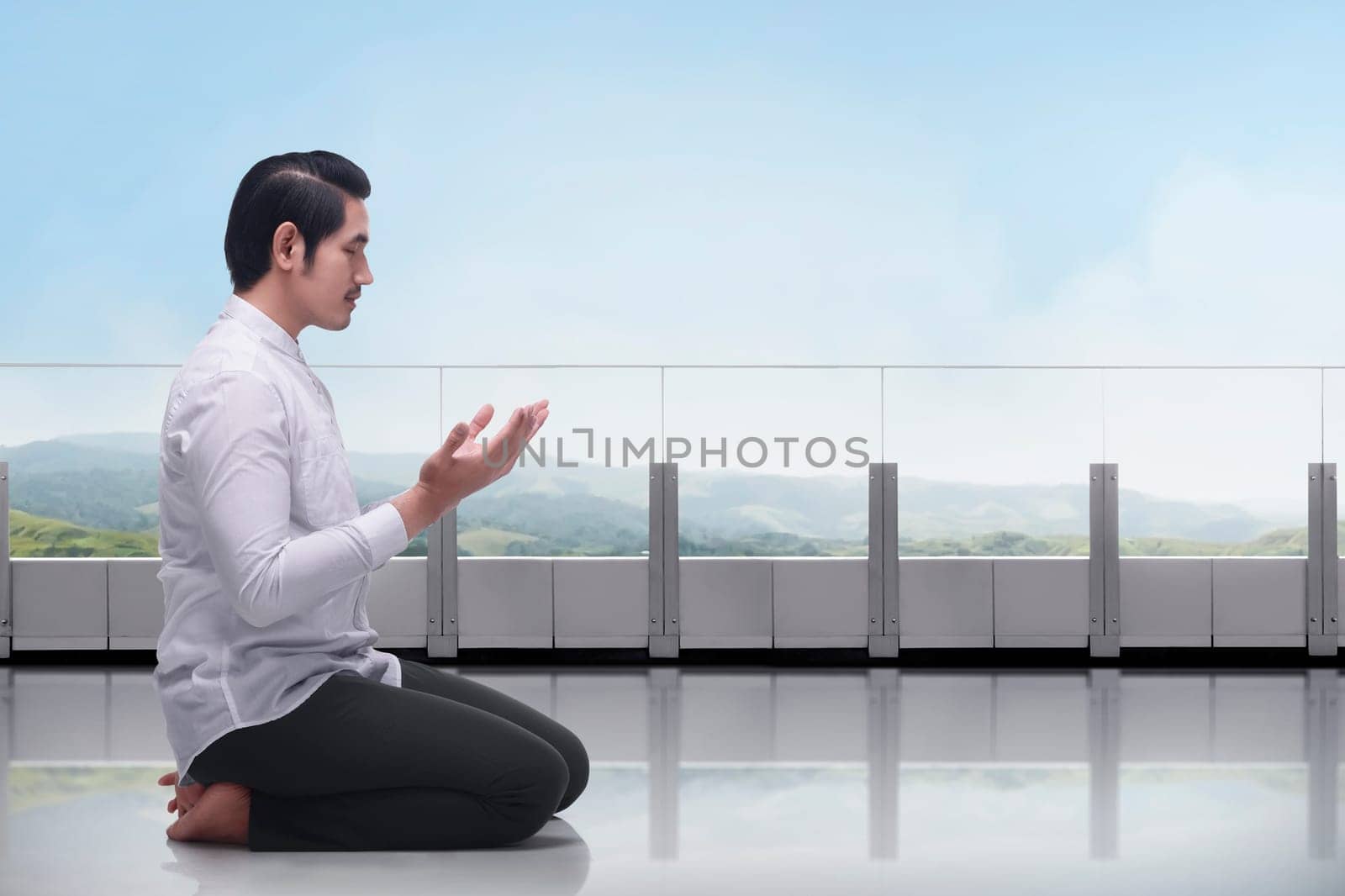 Young asian muslim man sitting in the terrace praying with blue sky background