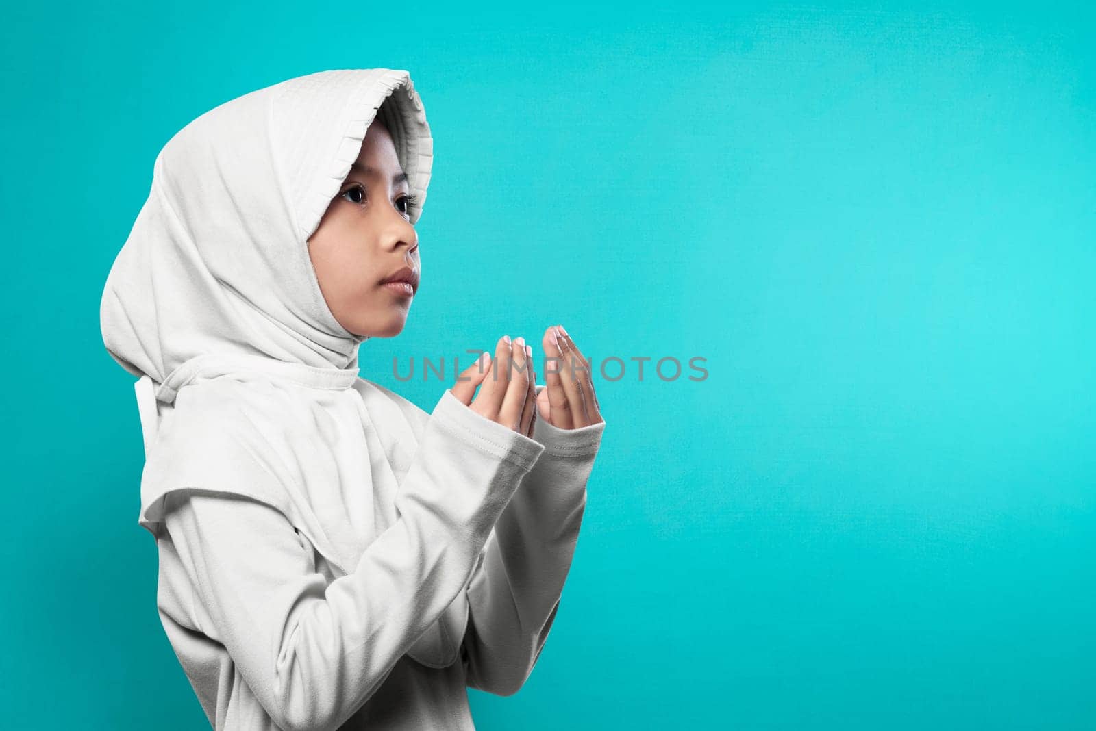 Asian muslim girl in hijab raising hand and praying over blue background
