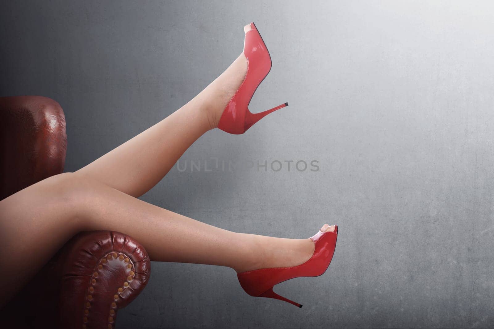 Sexy woman legs in red high heels on a couch at black wall background