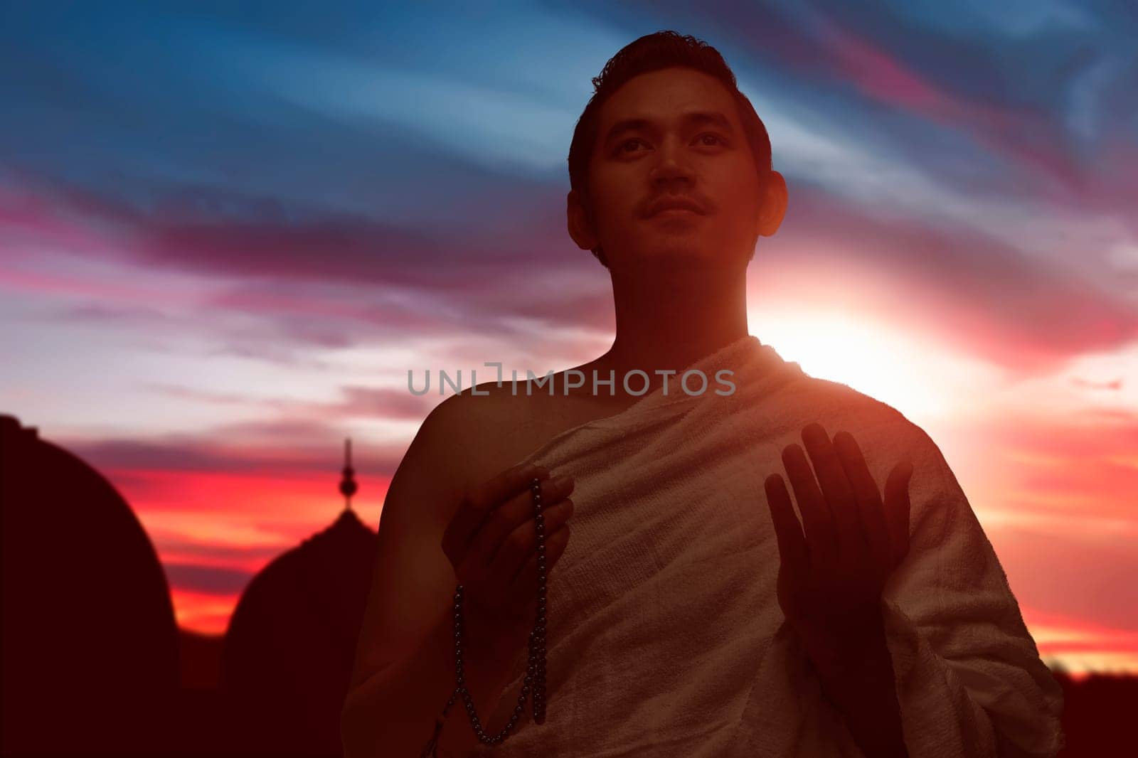Asian muslim man with ihram clothes praying to god over sunset background