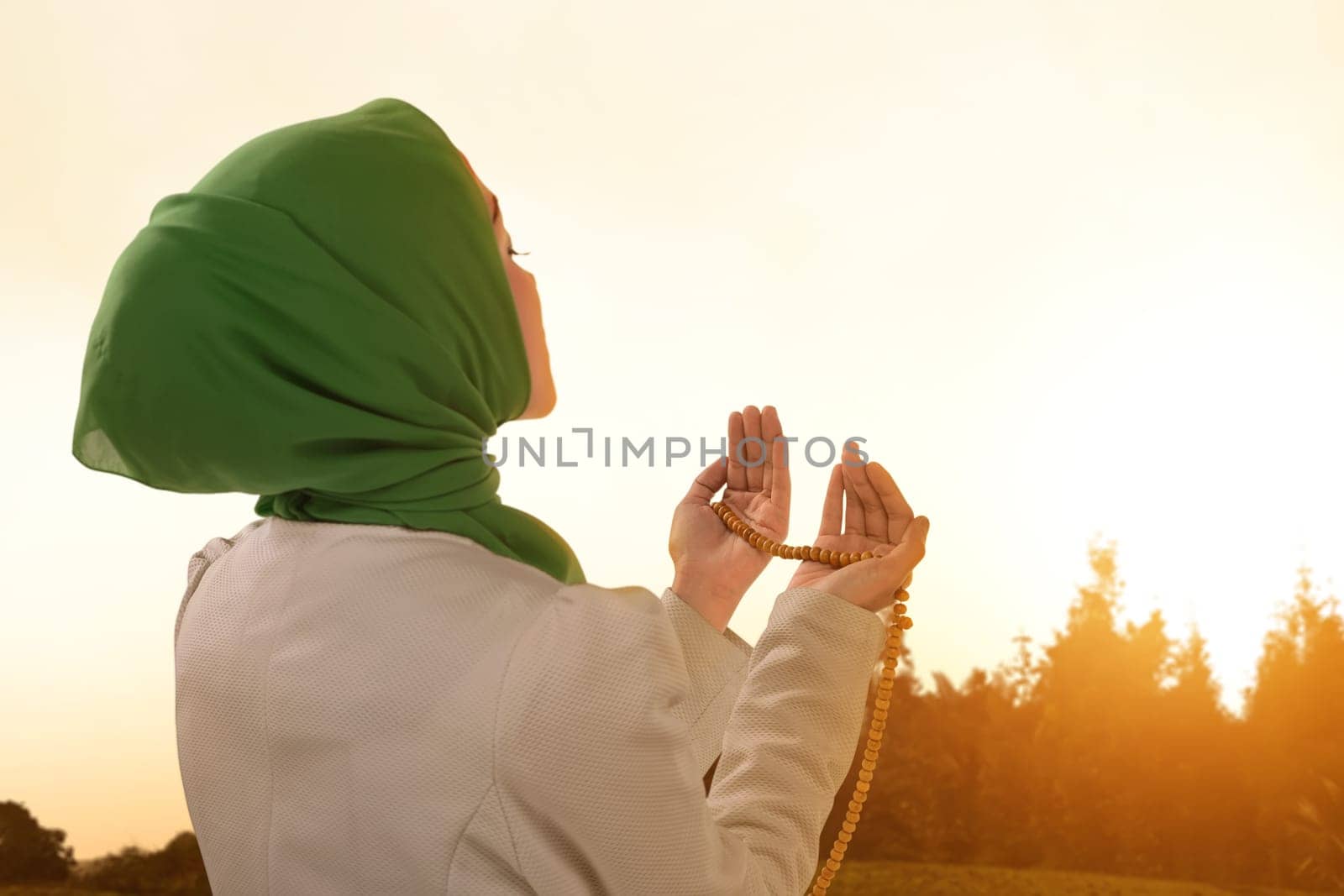 Beautiful asian muslim woman praying with prayer beads during sunset