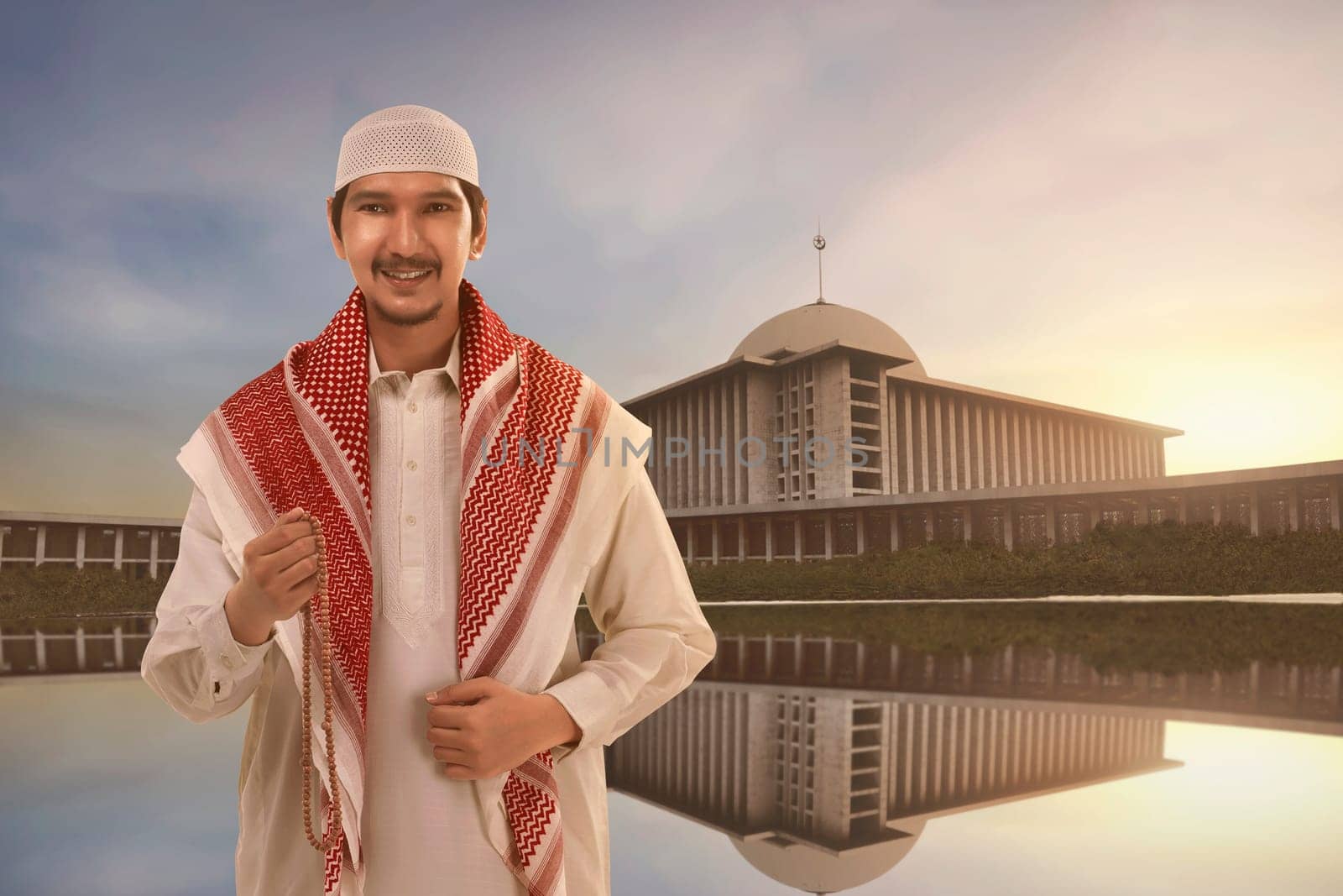 Handsome asian muslim man with traditional dress holding prayer beads against mosque background