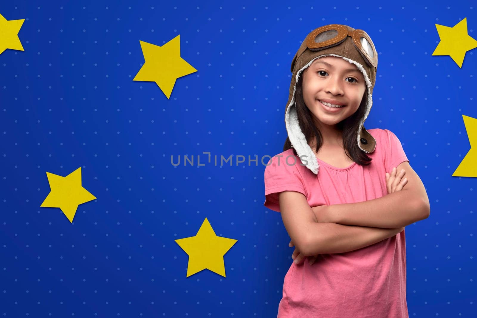 Funny asian little girl in astronaut costume standing over bright blue wall with yellow stars background