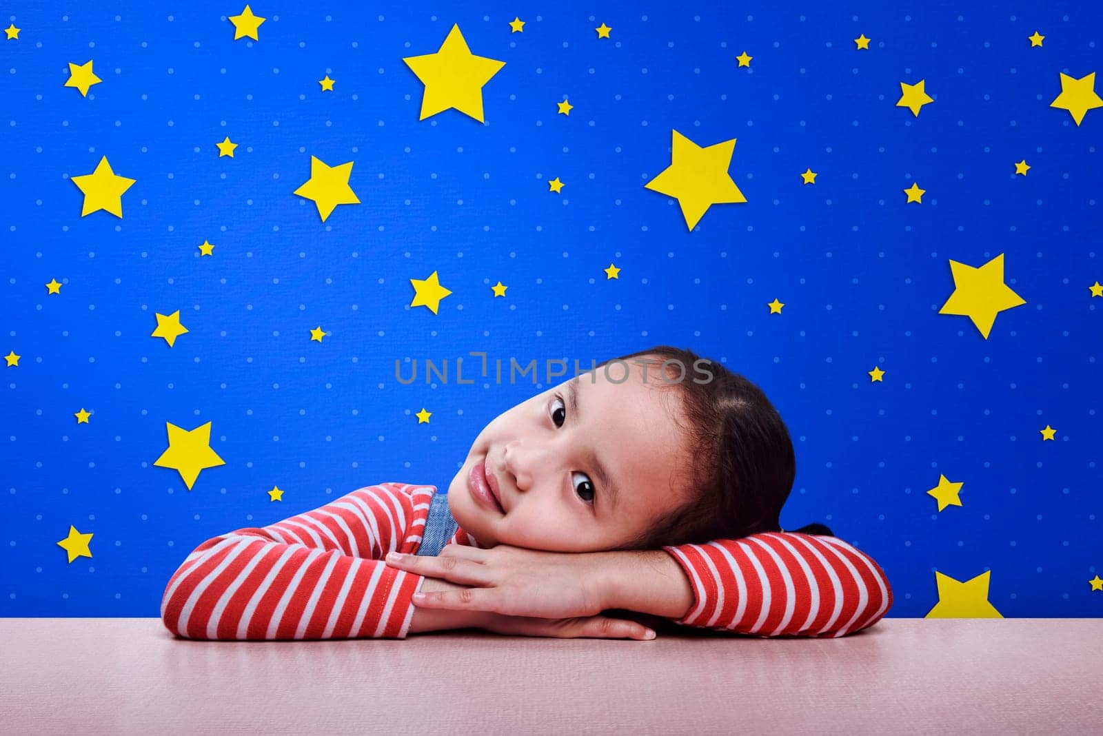 Smiling asian child resting on desk with yellow star on blue wall background