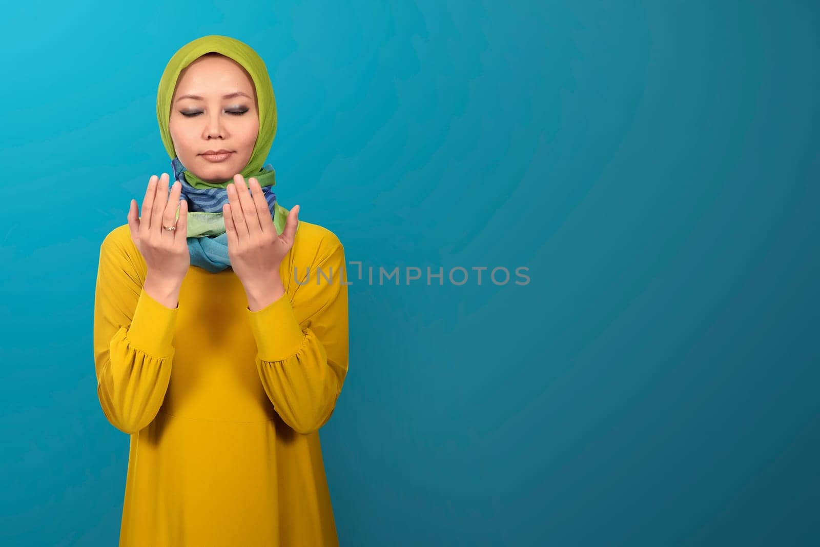 Beautiful asian muslim female praying against blue background