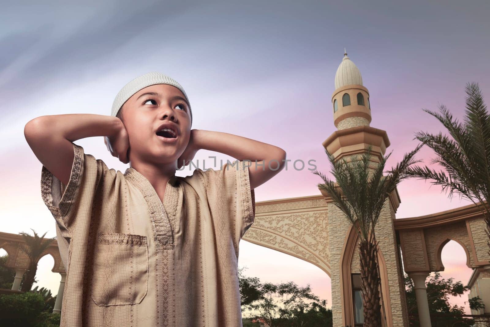 Asian muslim child with traditional dress praying against sky background