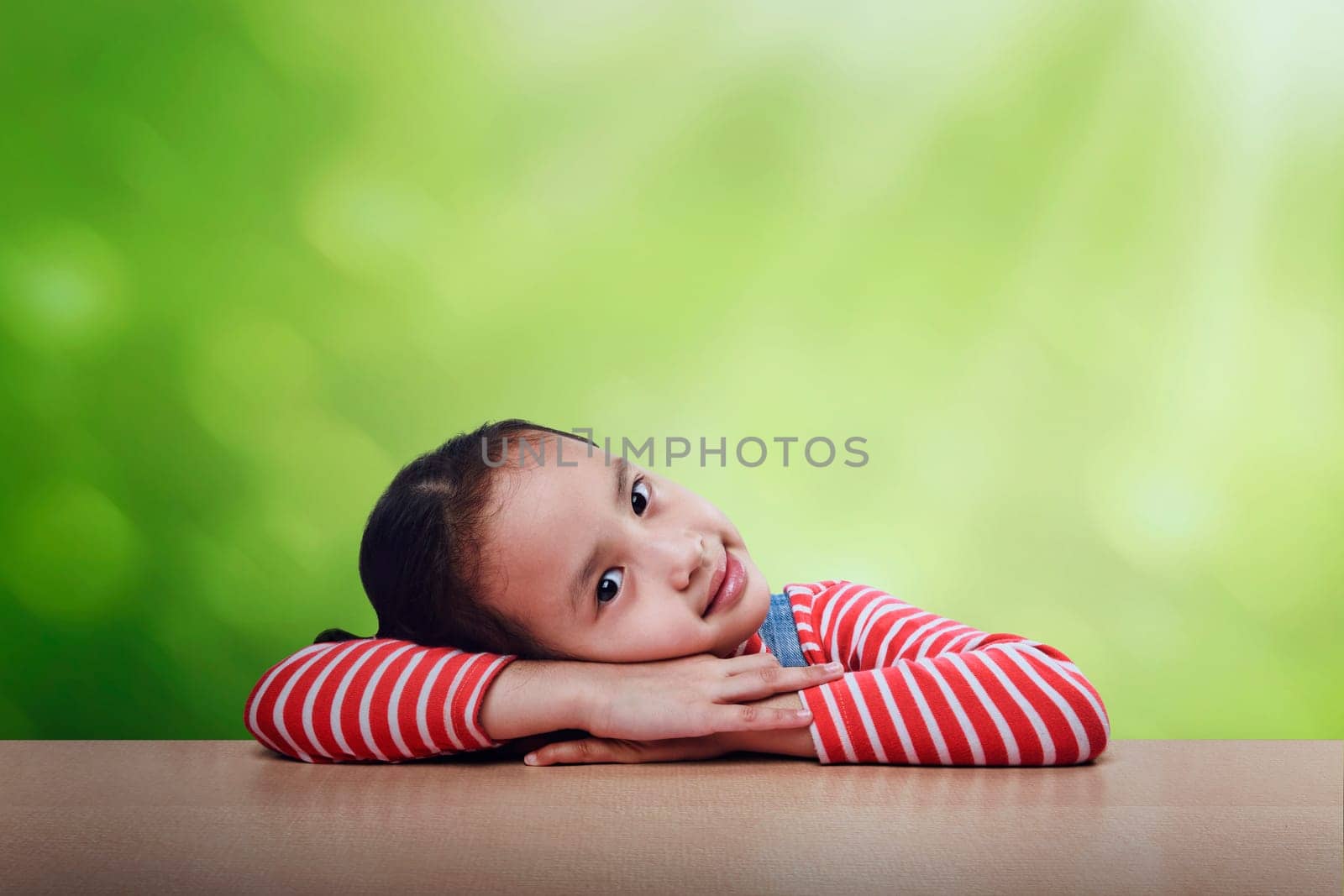 Cheerful asian kid lying down on the table over green background