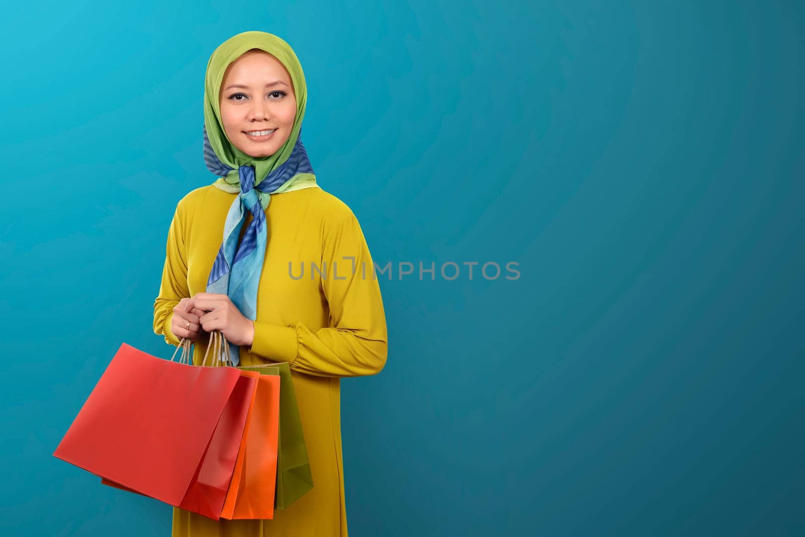 Young asian Muslim woman with shopping bag on blue background