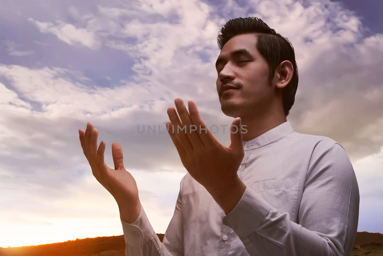 Young asian muslim man praying over sunset background