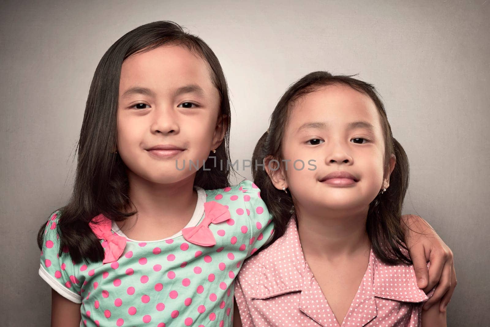 Portrait of asian little girl embracing her sister over grey background