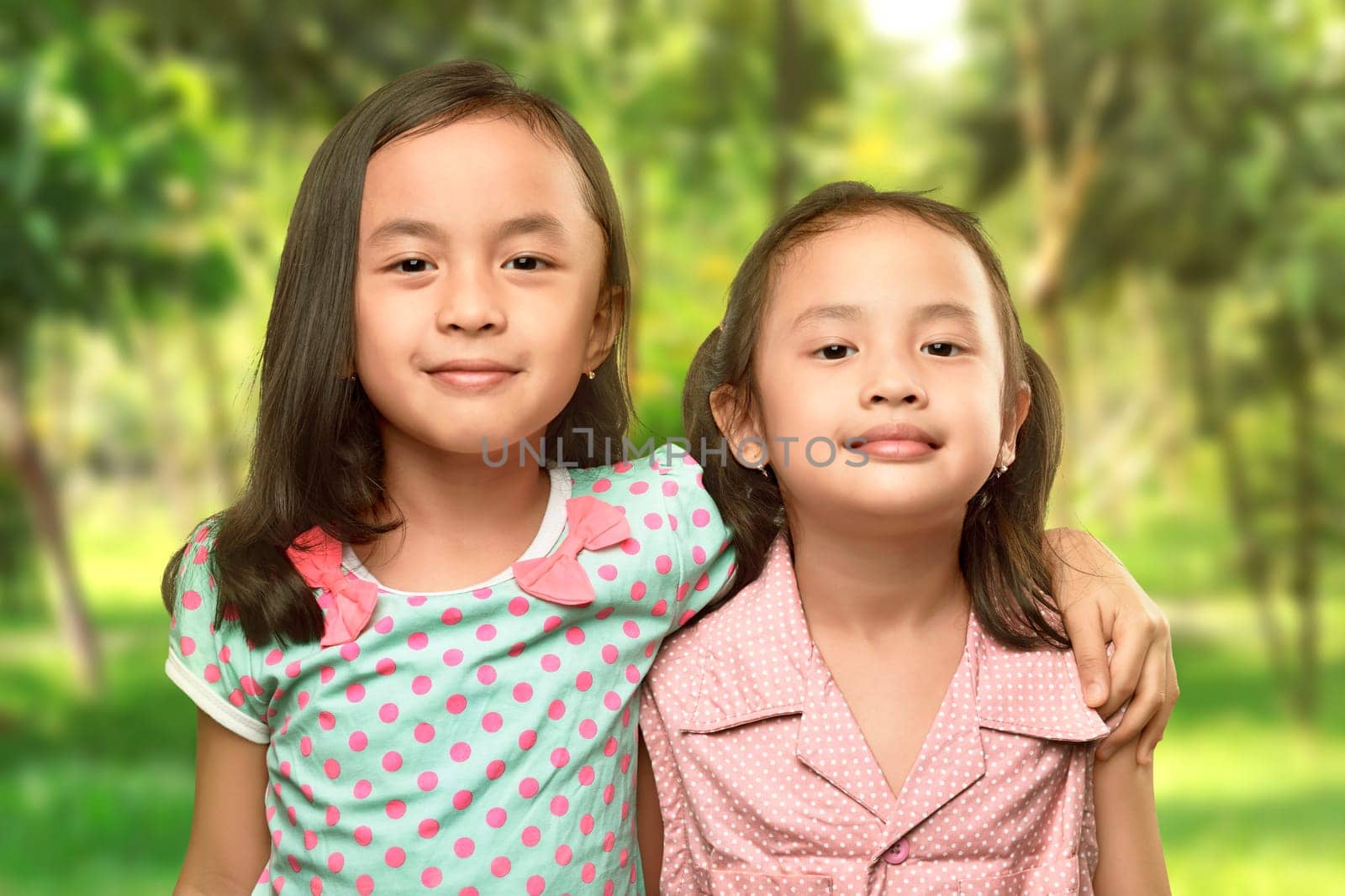 Funny two little sisters standing and hugging on the park