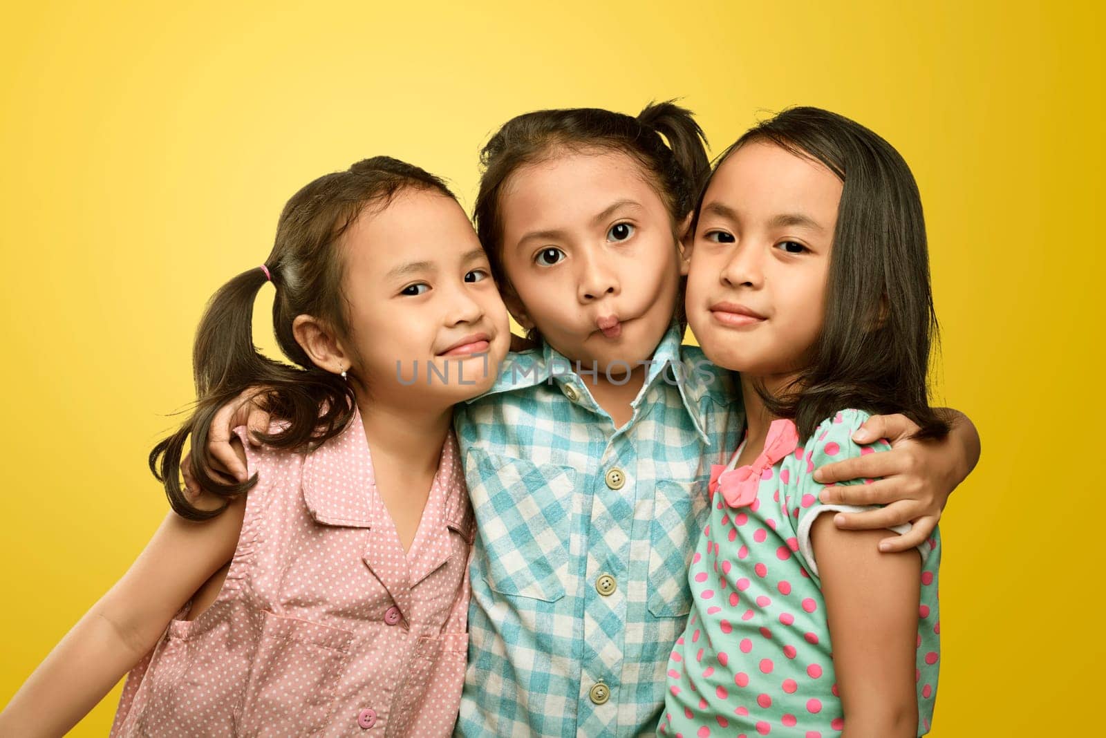 Happy group of asian little girl standing together over yellow background
