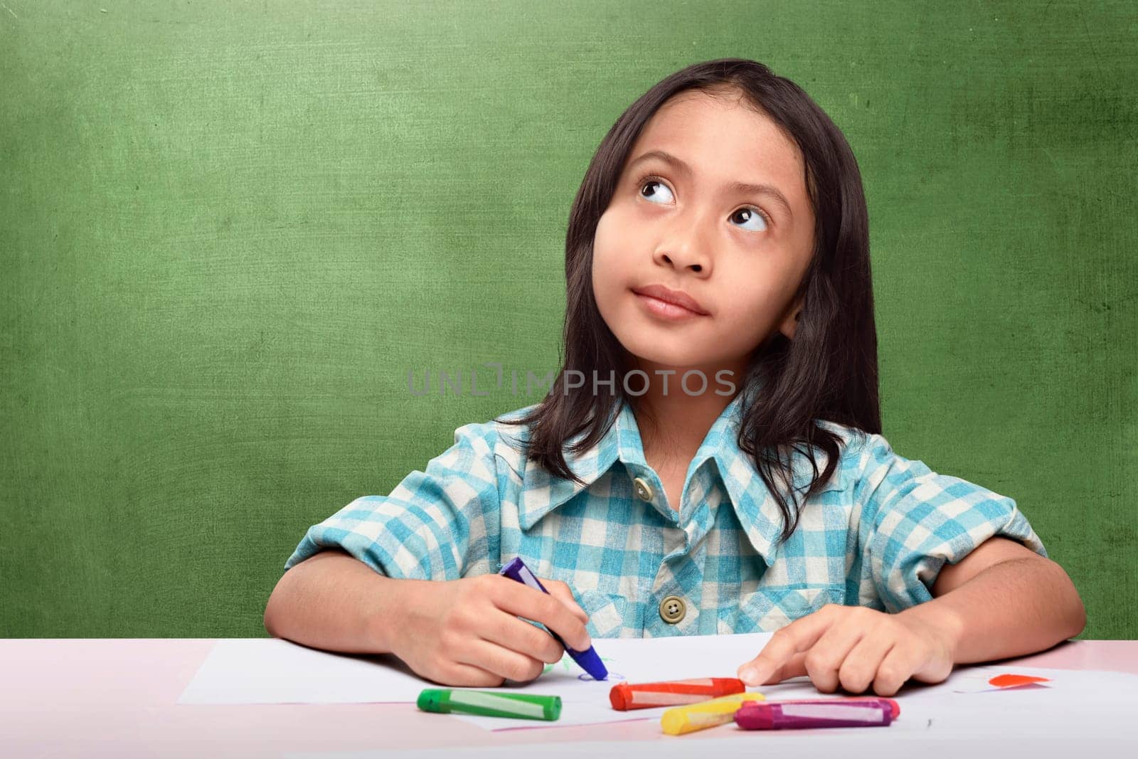 Cheerful asian child imagining something to drawing with crayon at school