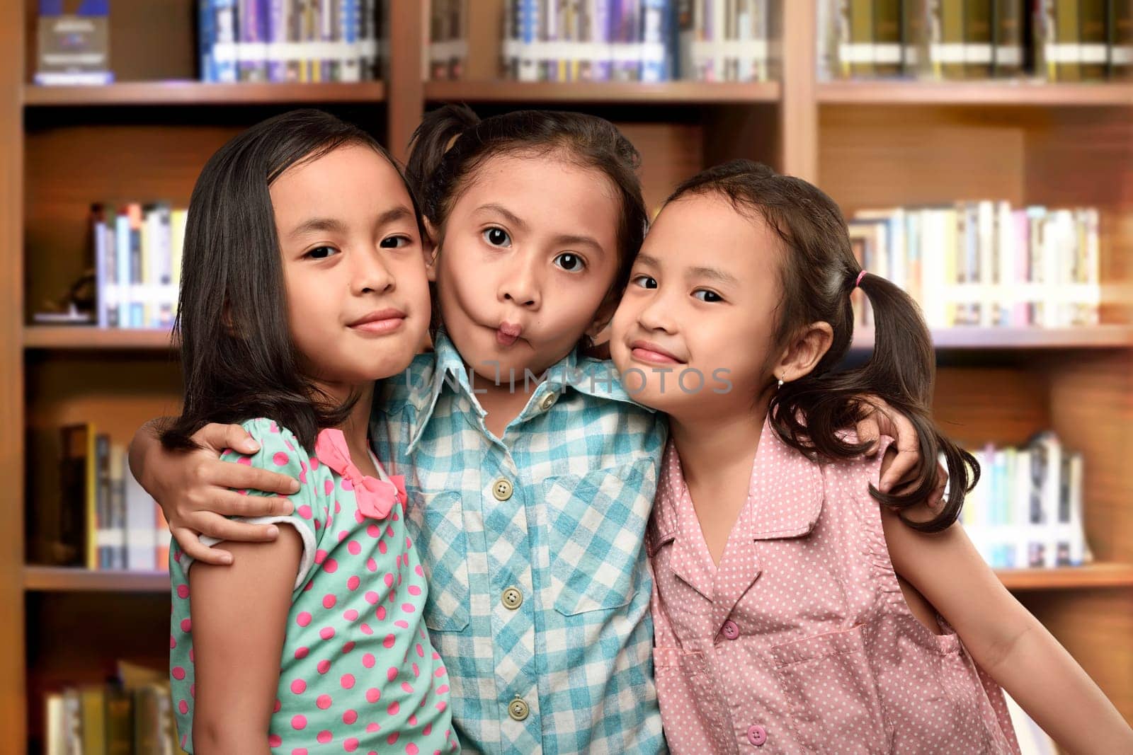 Group of happy asian kids playing and standing together against rack of book background