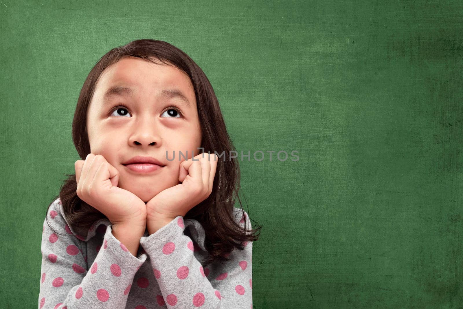 Beautiful asian little girl with hands in chin imagine something against chalkboard background