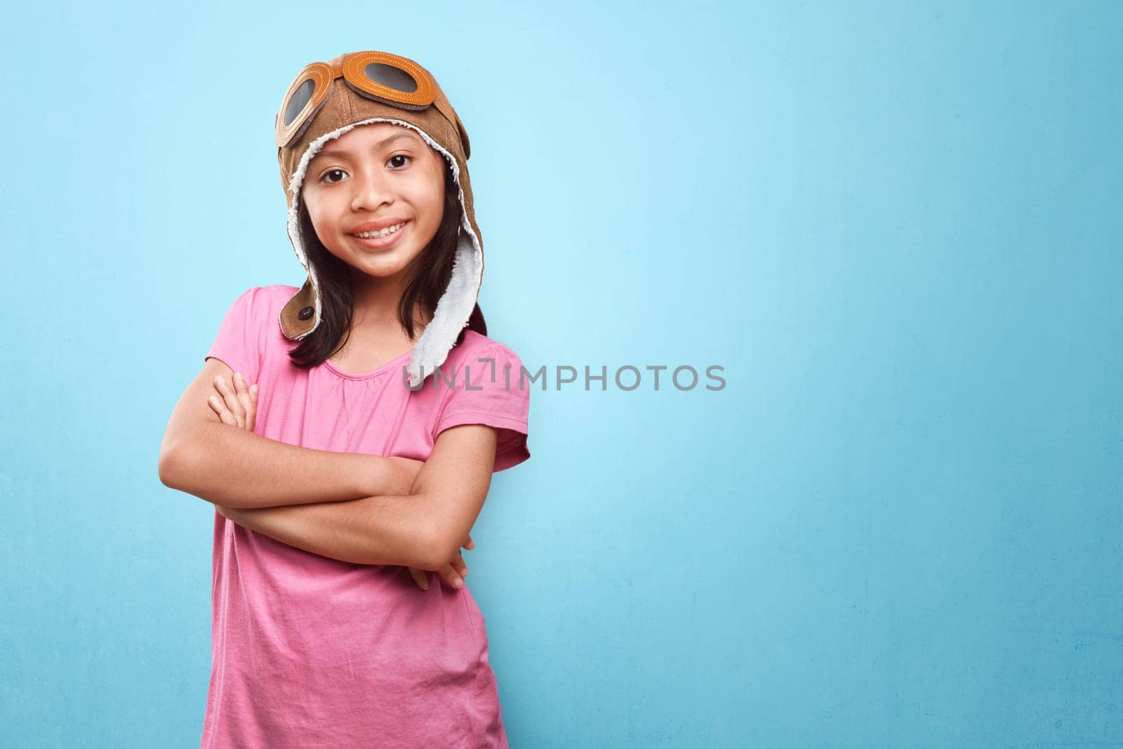 Smiling asian little girl with aviator hat and goggles having fun over blue background