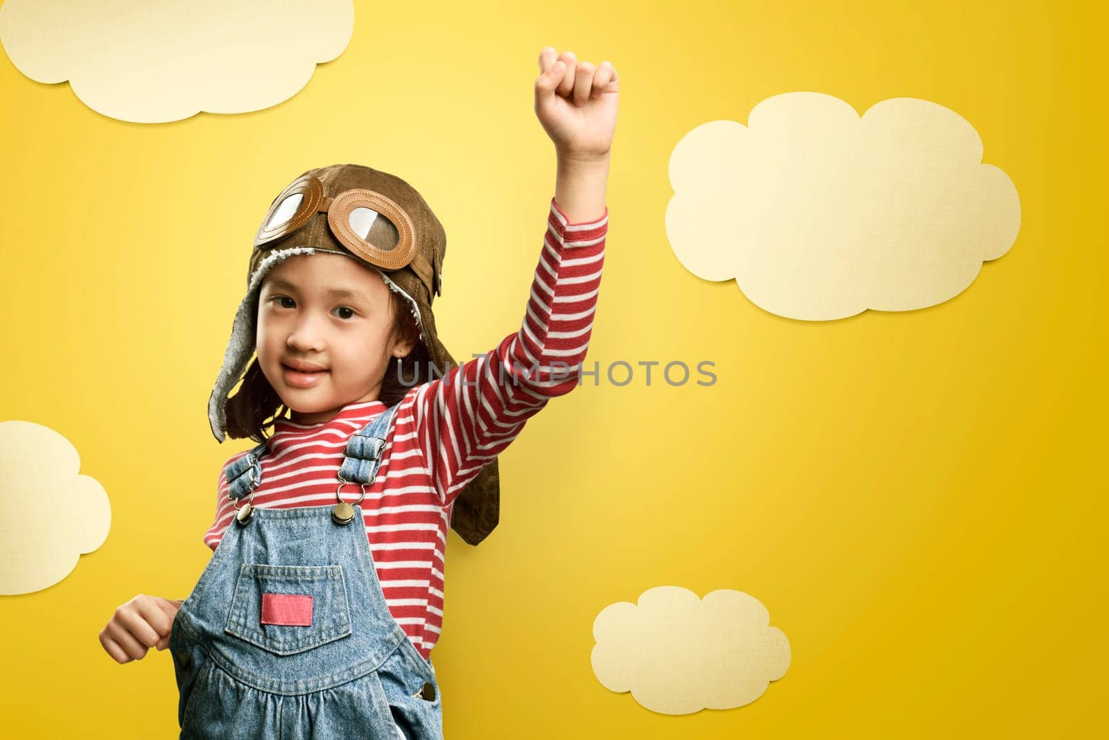 Cheerful asian kid with aviator hat and goggles having fun over yellow background