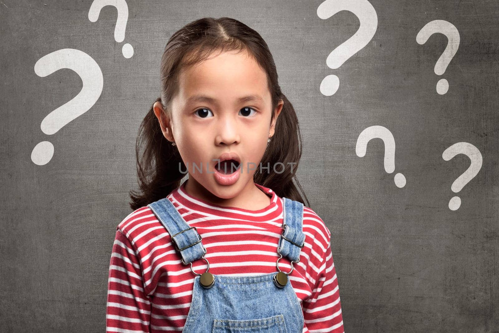 Cheerful asian child expression with question mark above her head over blackboard background