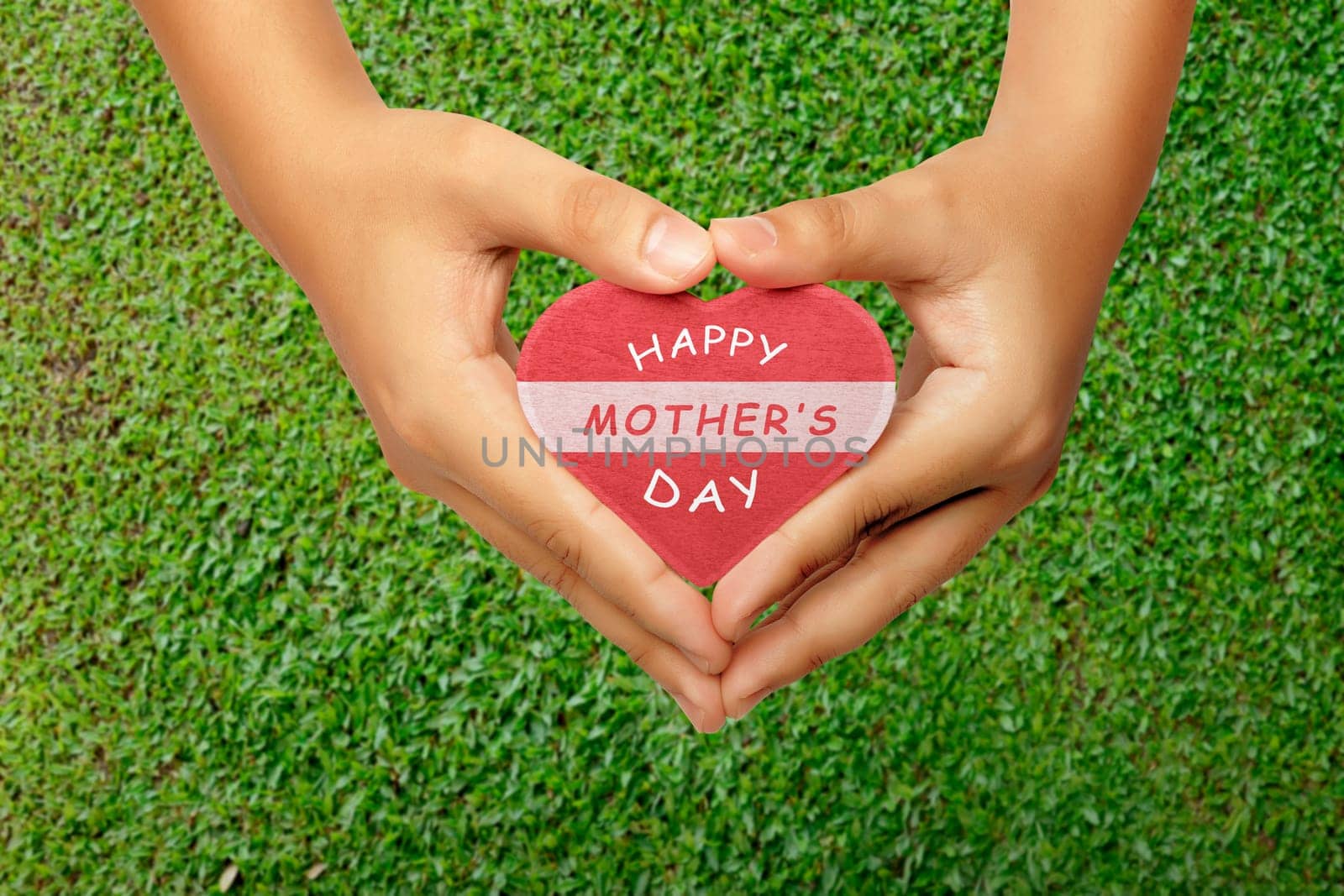 People hand holding heart with Happy Mothers day greeting on grass