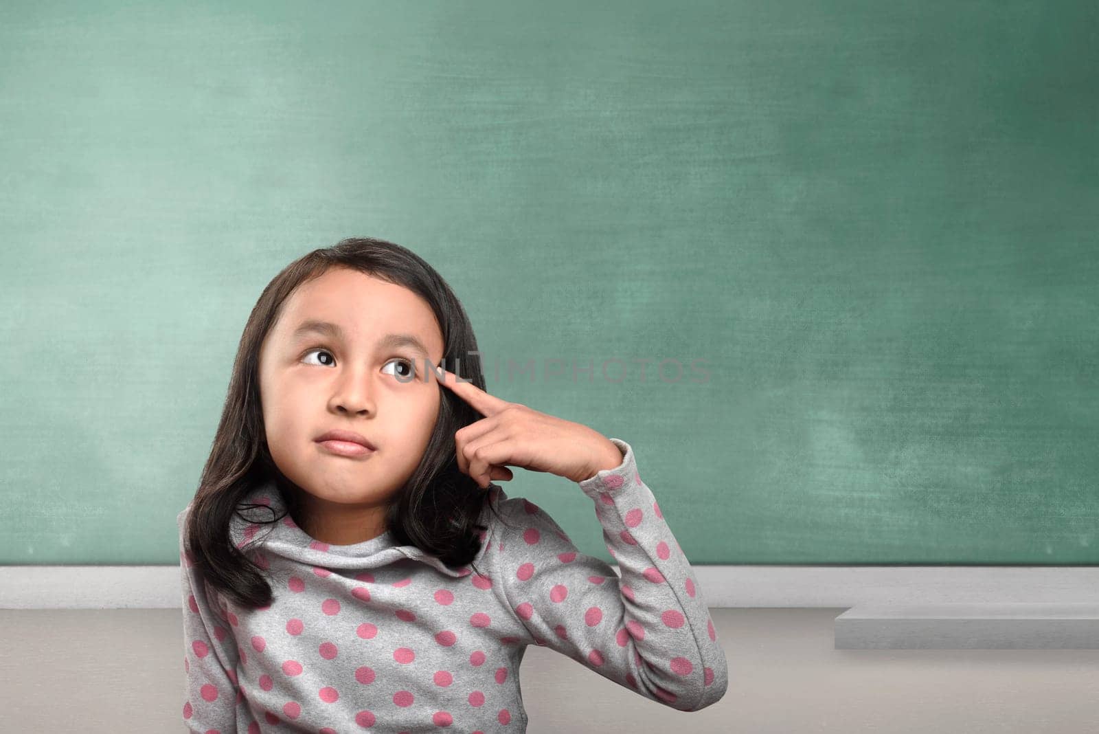 Happy asian girl thinking with pensive expression against chalkboard background