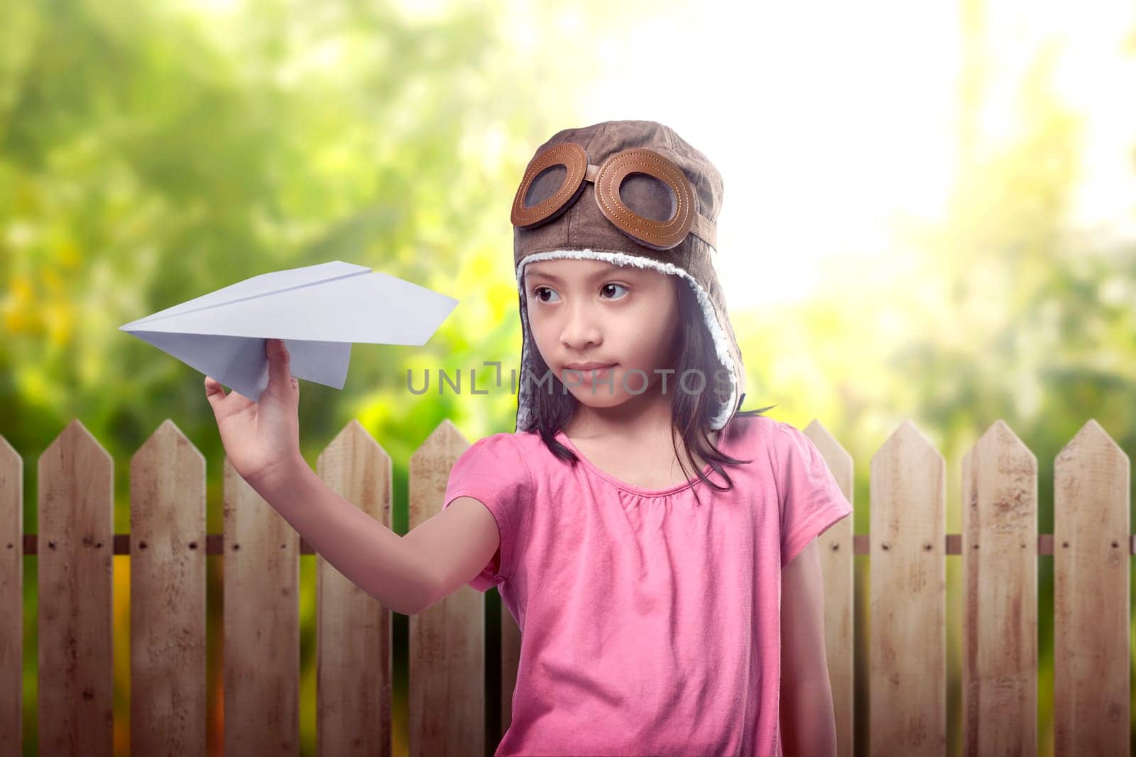 Funny asian little girl in aviator helmet playing toy airplane on the field