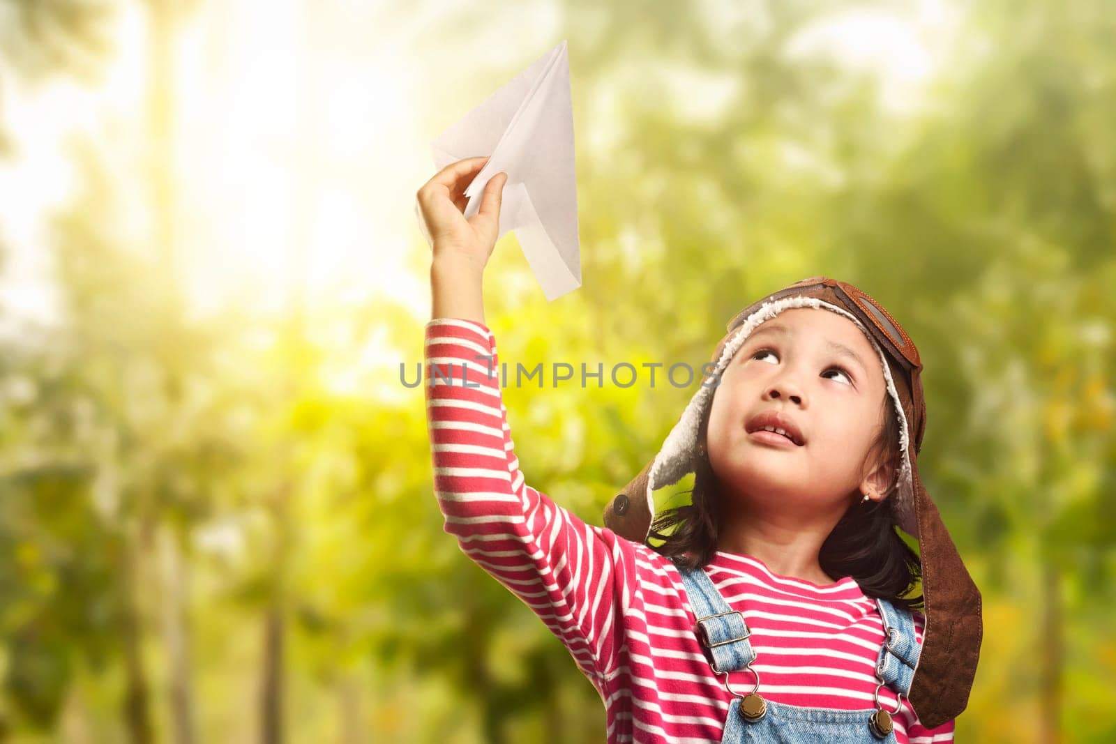 Cheerful asian child playing with paper plane on the park